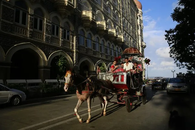 In this June 9, 2015 photo, a family enjoys a ride on a horse drawn carriage popularly known as “Victoria carriage” outside the Taj Mahal hotel in Mumbai, India. (Photo by Rafiq Maqbool/AP Photo)