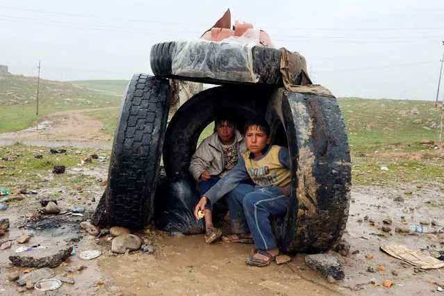 Displaced Iraqi people shelter from the rain on the street near the city of Mosul, Iraq, March 23, 2017. (Photo by Youssef Bouldlal/Reuters)