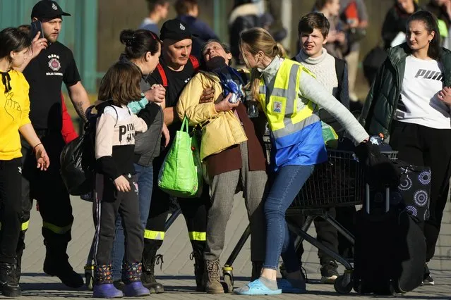 A woman losing her consciousness, receives help from Polish paramedics as other Ukrainian refugees pass the border crossing in Medyka, southeastern Poland, on Wednesday, March 23, 2022. (Photo by Sergei Grits/AP Photo)