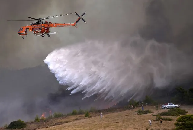 An helicopter drops water over a fire in Siderina village helicopter about 55 kilometers (34 miles) south of Athens, Greece, Monday, August 16, 2021. Greek authorities have deployed dozens of firefighters, as well as six water-dropping planes and four aircraft to a wildfire that broke out Monday morning in the Keratea region southeast of Athens, near the national park of Sounion. (Photo by Thanassis Stavrakis/AP Photo)