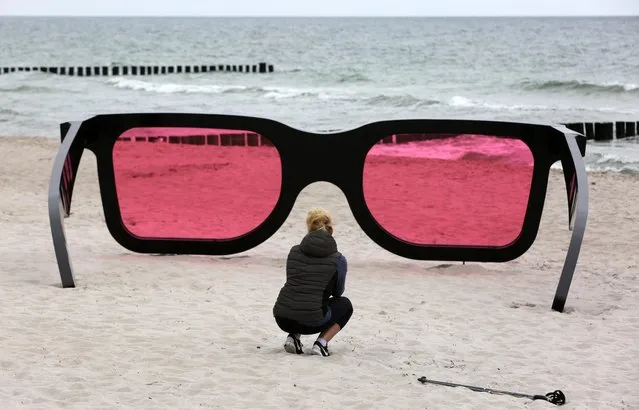 A woman takes a close look at oversized glasses titled “Sea Pink II” by Marc Moser at the Baltic Sea beach in Zingst, northern Germany, Thursday, May 26, 2016. The installation is part of the Environmental Photo Festival “Horizonte” in Zingst from May 28 to June 5, 2016. The festival consists of more than 20 exhibitions, workshops, a photo school and other different events. (Photo by Bernd Wuestneck/DPA via AP Photo)