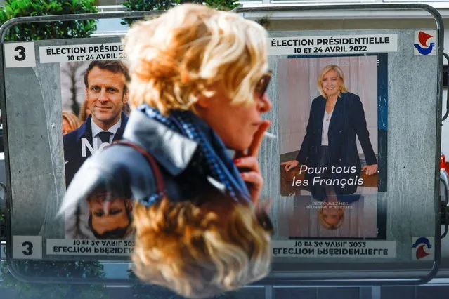 A woman walks past official campaign posters of French presidential election candidates Marine le Pen, leader of French far-right National Rally (Rassemblement National) party, and French President Emmanuel Macron, candidate for his re-election, displayed on an official billboard in Paris, France, April 19, 2022. (Photo by Gonzalo Fuentes/Reuters)