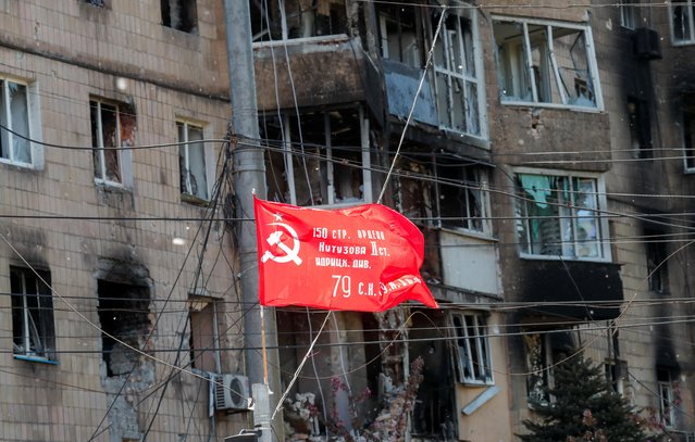 A Soviet-era flag, which was raised to mark the anniversary of the victory over Nazi Germany in World War Two, flies in front of a residential building heavily damaged in the course of Ukraine-Russia conflict in the southern port city of Mariupol, Ukraine on May 8, 2022. (Photo by Alexander Ermochenko/Reuters)