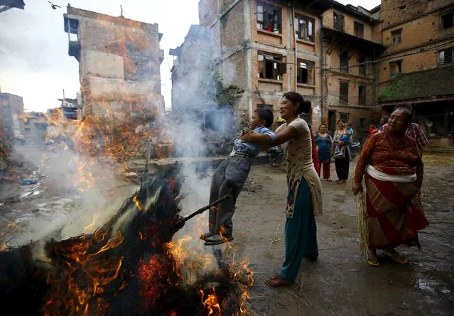 A woman swings a child around a fire, where an effigy of the demon Ghantakarna was burnt to symbolize the destruction of evil, during the Ghantakarna festival at the ancient city of Bhaktapur, Nepal August 12, 2015. (Photo by Navesh Chitrakar/Reuters)