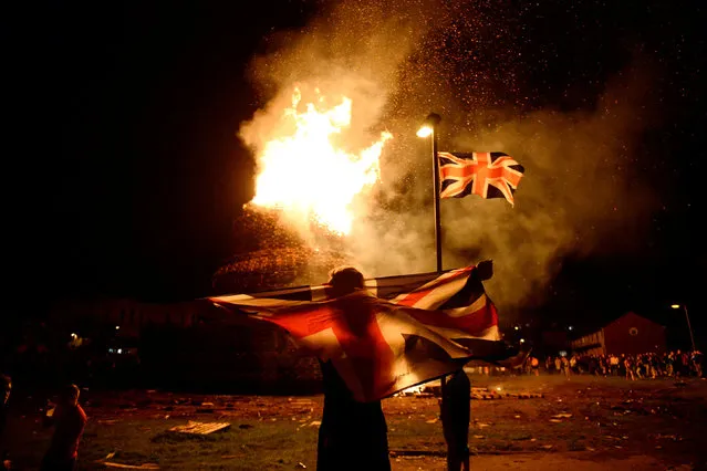 A boy holds a Union Jack flag in front of a bonfire burning in the Shankill Road area ahead of the Twelfth of July celebrations held by members of the Orange Order in Belfast, Northern Ireland, July 12, 2016. (Photo by Clodagh Kilcoyne/Reuters)