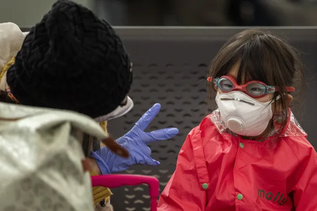 A woman plays with her daughter as they wait at Barcelona airport, Spain, Saturday, March 14, 2020. Spain's prime minister has announced a two-week state of emergency from Saturday in a bid to contain the new coronavirus outbreak. For most people, the new coronavirus causes only mild or moderate symptoms. For some, it can cause more severe illness, especially in older adults and people with existing health problems. (Photo by Emilio Morenatti/AP Photo)