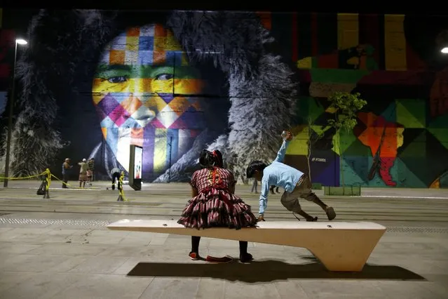 Locals sit in front of a mural created by Brazilian artist Eduardo Kobra that covers nearly 3,000 square meters of wall space Rio de Janeiro, Brazil on July 30, 2016. (Photo by Ivan Alvarado/Reuters)