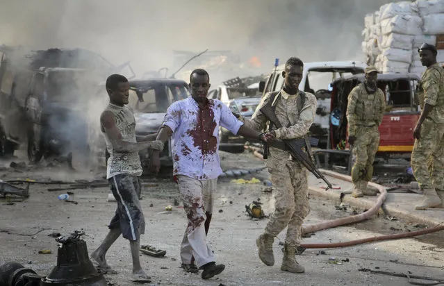 A Somali soldier helps a civilian who was wounded in a blast in the capital of Mogadishu, Somalia, Saturday, October 14, 2017. A huge explosion from a truck bomb has killed at least 20 people in Somalia's capital, police said Saturday, as shaken residents called it the most powerful blast they'd heard in years. (Photo by Farah Abdi Warsameh/AP Photo)
