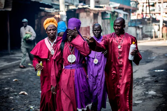 Members of the African church Legio Maria react while being affected by incoming tear gas canisters, during clashes between Kenyan Police and opposition supporters in Mathare, Nairobi on October 26, 2017. At least three people were shot dead October 26 and more than 30 wounded as opposition protesters clashed with police during Kenya' s presidential re- run, police and hospital sources said. (Photo by Luis Tato/AFP Photo)