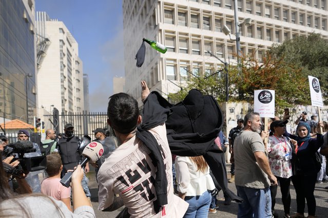 A protester throws a molotov cocktail at the Lebanese Central Bank building, background, where the anti-government demonstrators rally against the Lebanese Central Bank Governor Riad Salameh and the deepening financial crisis, in Beirut, Lebanon, Wednesday, October 5, 2022. (Photo by Hassan Ammar/AP Photo)