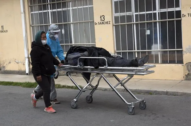 A healthcare worker dressed in protective gear pushes the body of a man to the spot where his family will wait for a funeral home to take him away, outside the General Hospital in La Paz, Bolivia, Thursday, July 23, 2020. According to a hospital health worker, the man died of COVID-19. (Photo by Juan Karita/AP Photo)