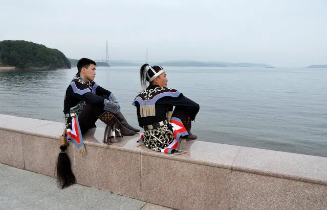 Participants, dressed in traditional costumes of ethnic groups inhabiting Chukotka region, sit on an embankment barrier shortly before the closing of the Eastern Economic Forum, with a bridge linking Russky Island with the mainland seen in the background, in Vladivostok, Russia, September 3, 2016. (Photo by Yuri Maltsev/Reuters)