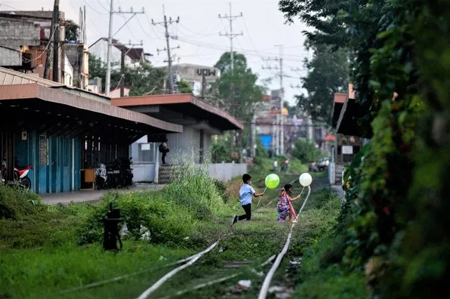 Children holding balloons cross railroad tracks, in Manila, Philippines on November 22, 2022. (Photo by Lisa Marie David/Reuters)