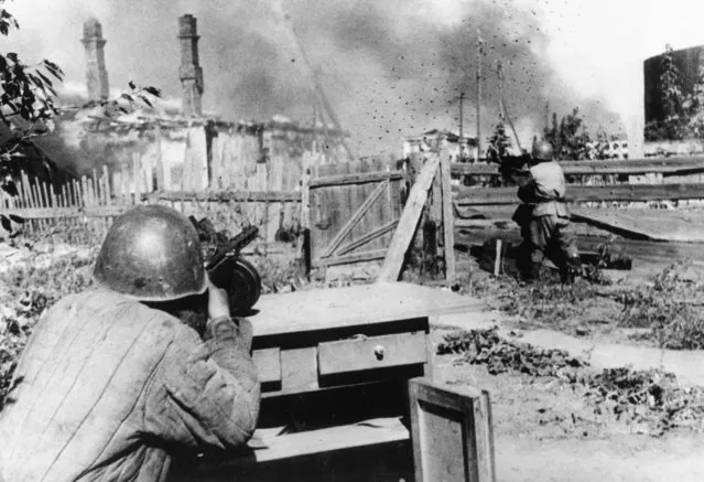 Standing in the backyard of an abandoned house in the outskirts of the besieged city of Leningrad, a rifleman of the Red Army aims and fires his machine gun at  German positions, on December 16, 1942. (Photo by AP Photo)