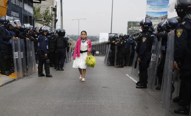 A girl walks past riot policemen guarding one of the access roads to Benito Juarez International airport after demonstrators staged a protest over the 43 missing Ayotzinapa students in Mexico City November 20, 2014. Forty-three missing students abducted by corrupt police in southwest Mexico weeks ago were apparently incinerated by drug gang henchmen and their remains tipped in a garbage dump and a river, the Mexican government said. (Photo by Tomas Bravo/Reuters)