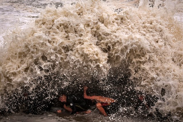 Young men crouch behind a wall as they play in record-breaking waves caused by the outer fringe of Tropical Cyclone Alfred at Point Danger in Coolangatta on March 7, 2025. Violent winds toppled power lines on March 7 as Tropical Cyclone Alfred inched towards Australia's eastern coast, sparking evacuation orders and leaving more than 50,000 homes without electricity. (Photo by David Gray/AFP Photo)