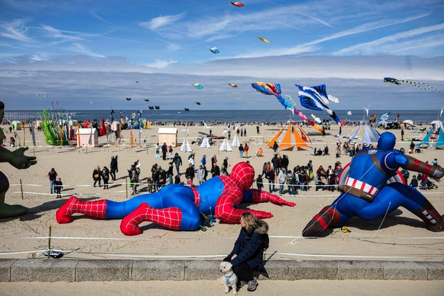A woman watches people flying kites during the 37th International Kite Festival (RICV) at the beach of Berck-sur-Mer, northern France, on April 23, 2024. (Photo by Sameer Al-Doumy/AFP Photo)