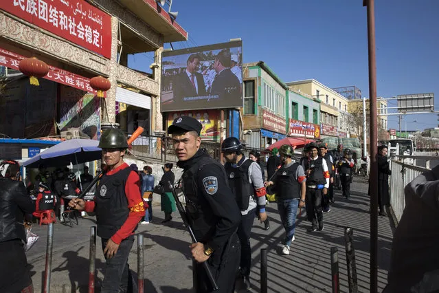 In this November 3, 2017 file photo, armed civilian patrol the area outside the Hotan Bazaar where a screen shows Chinese President Xi Jinping in Hotan in western China's Xinjiang region.  Tibetan activists, housing petitioners and other campaigners are targets of a new national campaign in China against so-called organized crime. The sweep expands the range of people law enforcement officials can take into custody in the name of preserving peace and order. Analysts say the crackdown will help President Xi Jinping win political support in counties and villages, boosting his legitimacy as he prepares to rule the country indefinitely. (Photo by Ng Han Guan/AP Photo)