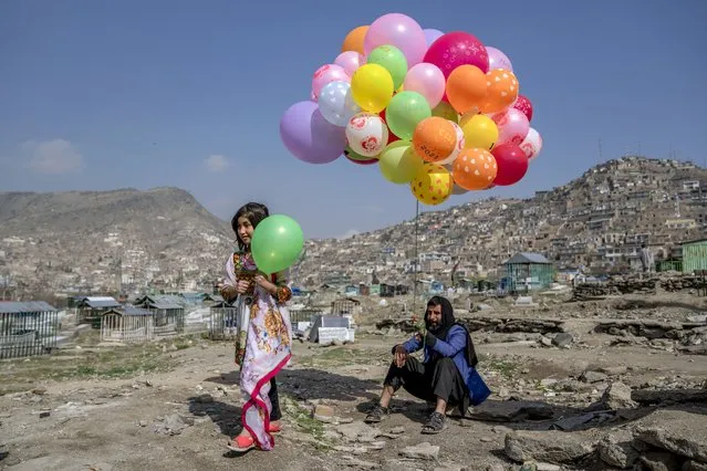 A girl buys a ballon from a ballon seller, during celebration of Nowruz, the Persian New Year, in a cemetery in Kabul, Afghanistan, Tuesday, March 21, 2023. Nowruz is celebrated on the first day of spring in countries including Afghanistan, Tajikistan, and Iran. (Photo by Ebrahim Noroozi/AP Photo)