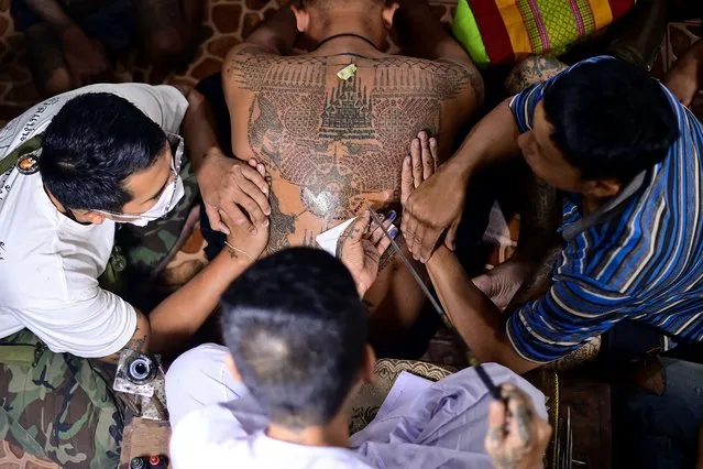 A Buddhist devotee (C) gets a traditional “Sak Yant” tattoo during an annual sacred tattoo festival at the Wat Bang Phra temple in Nakhon Pathom province on March 4, 2023. (Photo by Manan Vatsyayana/AFP Photo)