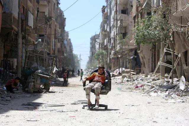 A boy sits on a chair along a damaged street at the city of Douma in Damascus, Syria April 16, 2018. (Photo by Ali Hashisho/Reuters)