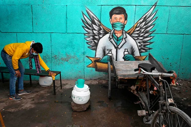 A vendor of a roadside eatery stall cleans a bench for customers in front of a mural representing a frontline warrior of the Covid-19 coronavirus, painted on a wall in New Delhi on December 27, 2020. (Photo by Sajjad Hussain/AFP Photo)