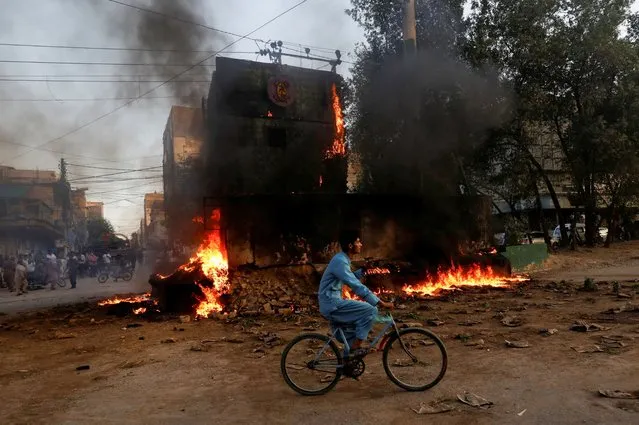 A boy rides past a paramilitary check post, that was set afire by the supporters of Pakistan's former Prime Minister Imran Khan, during a protest against his arrest, in Karachi, Pakistan on May 9, 2023. (Photo by Akhtar Soomro/Reuters)