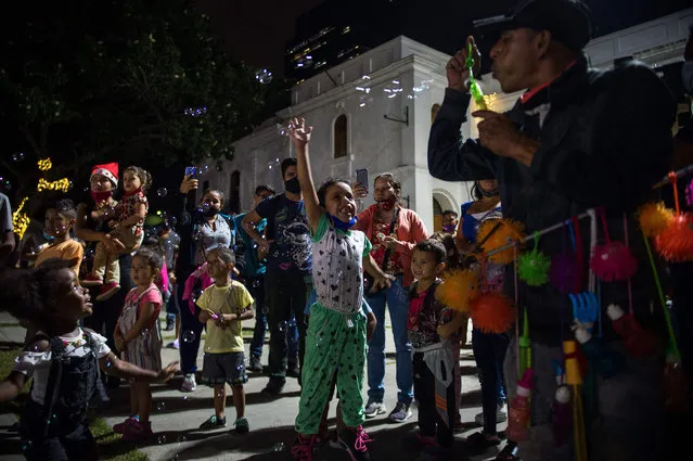 Children play with bubbles as people, some wearing face masks against the spread of the Covid-19, enjoy Christmas celebrations at a square in Caracas, on December 21, 2020. Venezuela abandoned its rigid controls to stop the spread of covid-19 for Christmas, and relaxed its confinement, but the measures anticipate a strong surge in contagions, according experts. (Photo by Cristian Hernandez/AFP Photo)