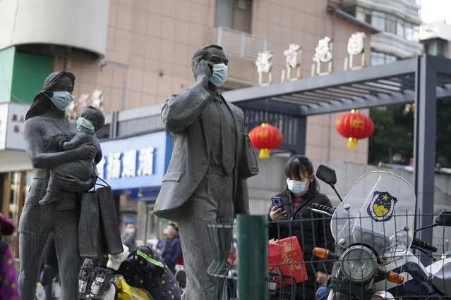 A woman wearing a mask walks past statues with masks placed on them in Wuhan in central China's Hubei province on Friday, January 29, 2021. A World Health Organization team is visiting the central city of Wuhan where the coronavirus was first detected. (Photo by Ng Han Guan/AP Photo)