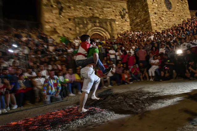 A man carries a young boy while walking on the burning embers during the night of San Juan in San Pedro Manrique, northern Spain, Sunday, June 24, 2018. The night of San Juan, which welcomes the summer season, is an ancient tradition celebrated every year in various towns in Spain. (Photo by Alvaro Barrientos/AP Photo)