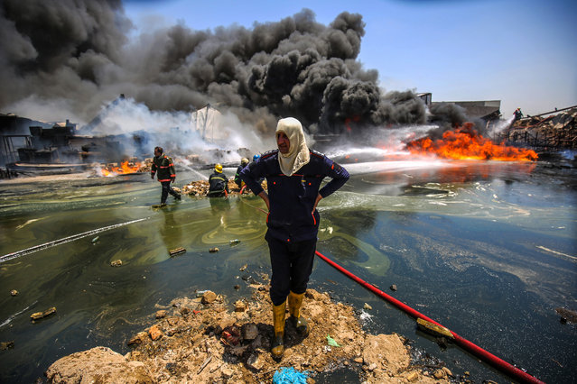 An Iraqi firefighter gazes during a blaze as comrades attempt to put out a fire that broke out due to extreme summer temperatures in a warehouses near Palestine Street in the capital Baghdad on July 10, 2018. The warehouses contained wood stocks, engine oils, pigments, and vehicle spare parts according to the civil defence. (Photo by Ahmad Al-Rubaye/AFP Photo)