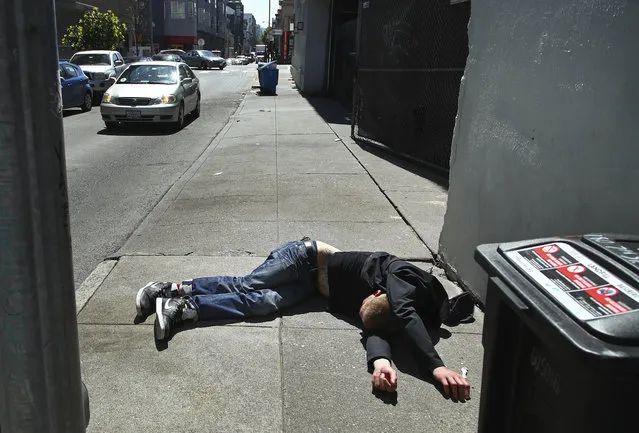 In this April 26, 2018, file photo, a man lies on the sidewalk beside a recyclable trash bin in San Francisco. San Francisco voters will decide in November 2018 whether to tax large businesses to pay for homeless and housing services in a city struggling with income inequality. Supporters collected enough signatures to get the measure on the ballot. (Photo by Ben Margot/AP Photo)