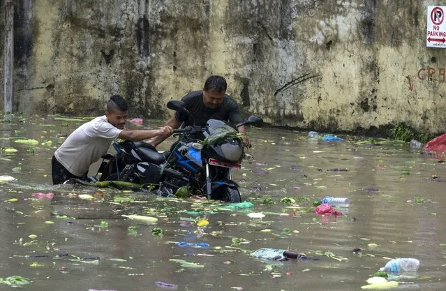 Two men push a motorcycle through flood waters after heavy monsoon rains flooded a vegetable market in Kathmandu, Nepal, Tuesday, August 8, 2023. (Photo by Niranjan Shrestha/AP Photo)