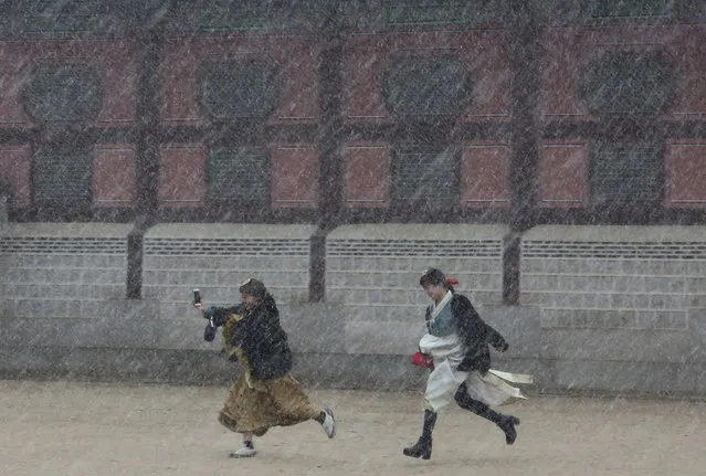 Women wearing South Korean traditional costume “Hanbok” run from the sudden snow fall at the Gyeongbok Palace, the main royal palace during the Joseon Dynasty, in Seoul, South Korea, Wednesday, March 21, 2018. (Photo by Ahn Young-joon/AP Photo)