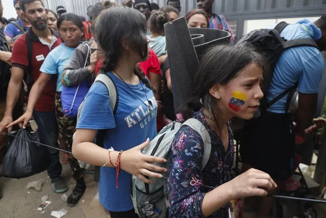 A migrant girl with the colors of the Venezuelan flag painted on her cheek lines up to acquire a Honduras Migration transit permit to continue on her way north to Guatemala and hopefully to the Mexico-United States border, in Danlí, Honduras, Wednesday, October 11, 2023. (Photo by Elmer Martinez/AP Photo)