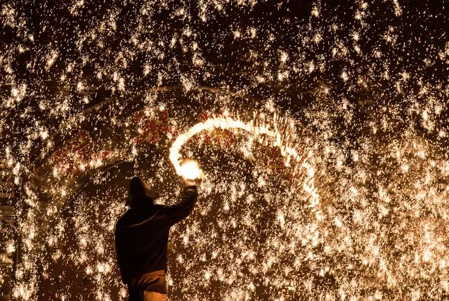 A Chinese blacksmith throws molten metal against a cold stone wall to create sparks, during the Lunar New Year celebration in Nuanquan, Hebei province on February 11, 2016. For over 300 years, the village has carried out the tradition of spraying molten iron at 1,300 degrees Celsius against a cold concrete wall to form spark-like fireworks during the Chinese New Year celebration, according to the organizer. (Photo by Johannes Eisele/AFP Photo)