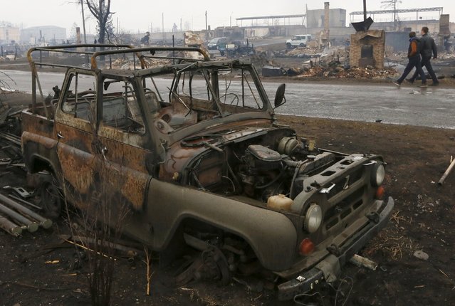 Men walk past a burnt vehicle in the settlement of Shyra, damaged by recent wildfires, in Khakassia region, April 13, 2015. (Photo by Ilya Naymushin/Reuters)