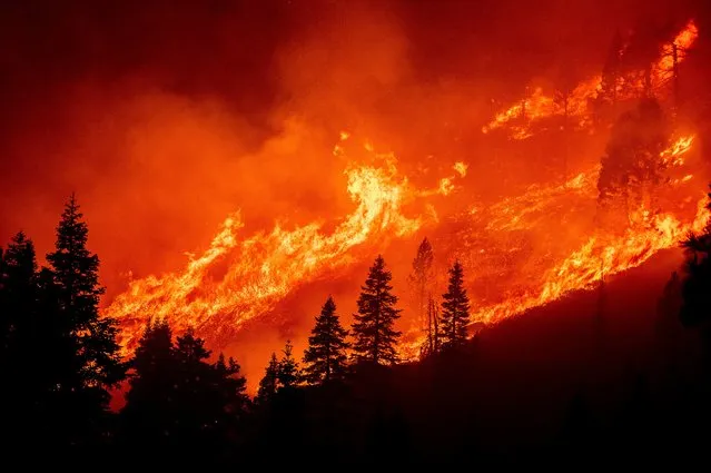 Seen from South Lake Tahoe, Calif., flames from the Caldor Fire leap along a hillside above Christmas Valley on Monday, August 30, 2021. (Photo by Noah Berger/AP Photo)