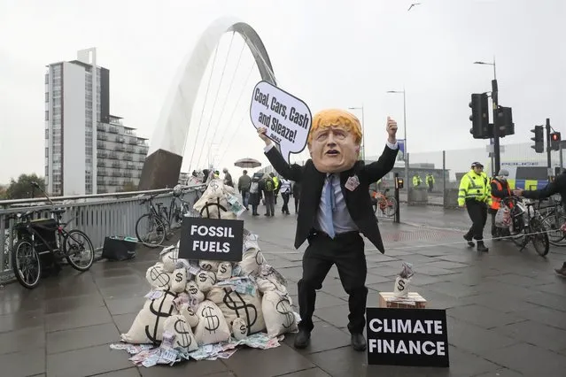 A protestor wears a caricature head of Britain's Prime Minister Boris Johnson during a protest near the venue of the COP26 U.N. Climate Summit in Glasgow, Scotland, Friday, November 12, 2021. (Photo by Scott Heppell/AP Photo)