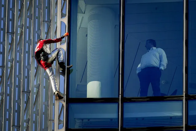 French urban climber Alain Robert climbs up the Skyper high-rise building in central Frankfurt, Germany, as a man watches from his office, Tuesday, November 23, 2021. (Photo by Michael Probst/AP Photo)