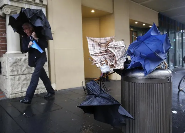 A man takes shelter next to discarded broken umbrellas in a litter bin during heavy rain in the Sydney central business district, Tuesday April 21, 2015 Sydney, Australia. (Photo by David Moir/AAP Image via AP Photo)