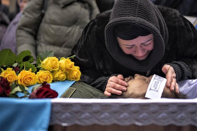 Roza cries over the body of her husband Oleksandr Maksymenko, 38, during his funeral in his home-village Kniazhychi, east of Kyiv, Ukraine, Monday, February 13, 2023. Oleksandr, a civilian who was a volunteer in the armed forces of Ukraine, was killed in the fighting in Bakhmut area. (Photo by Emilio Morenatti/AP Photo)