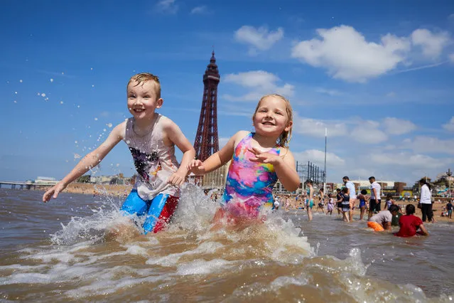 Charlie and Rosie Darwell jump the waves on Blackpool beach, England on July 23, 2019, as temperatures at the Lancashire coastal resort reached 28ºC. (Photo by  Christopher Thomond/The Guardian)