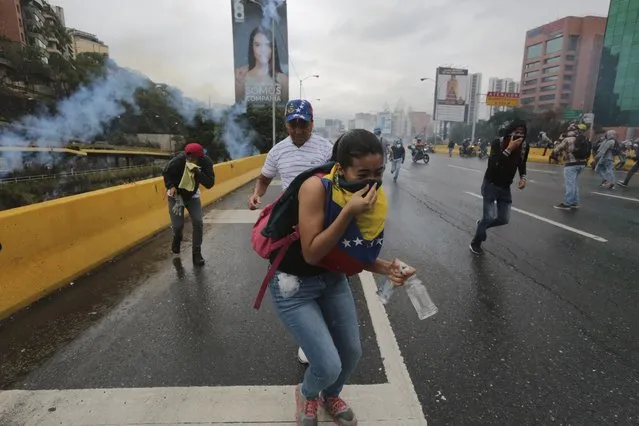 Demonstrators take cover from tear gas fired by Bolivarian National Guard soldiers during an anti-government protest in Caracas, Venezuela, Thursday, April 13, 2017. (Photo by Fernando Llano/AP Photo)