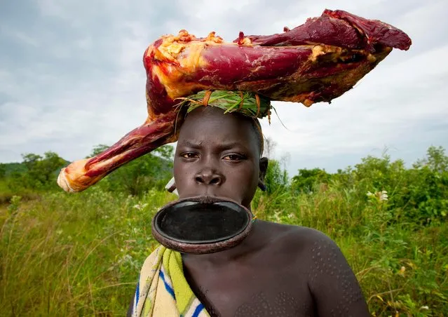 A tribeswoman sporting a huge lip plate and wearing a skinned animal carcass on her head. (Photo by Eric Lafforgue/Exclusivepix Media)