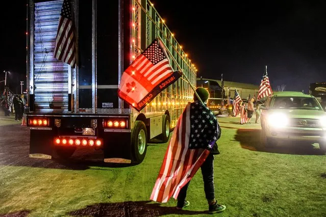 A person walks with American and Canadian flags while hundreds of vehicles including 18-wheeler trucks, RVs and other cars are parked as part of a rally at Hagerstown Speedway after some of them arrived as part of a convoy that traveled across the country headed to Washington D.C. to protest COVID-19 related mandates and other issues in Hagerstown, Maryland, March 5, 2022. (Photo by Stephanie Keith/Reuters)