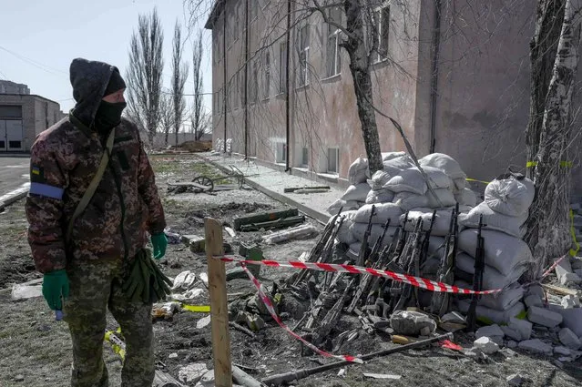A Ukranien soldier stands next to rifles of dead and injured soldiers close to the military school hit by Russian rockets the day before, in Mykolaiv, southern Ukraine, on March 19, 2022. (Photo by Bulent Kilic/AFP Photo)