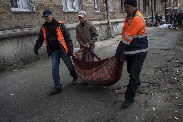Neighbours carry pieces of broken window from apartments damaged by shelling, in Kyiv, Ukraine, Wednesday, March 23, 2022. (Photo by Rodrigo Abd/AP Photo)
