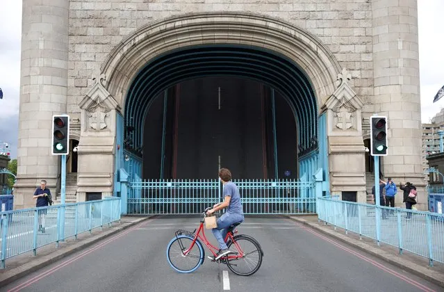 A cyclist looks towards Tower Bridge while it is stuck in the open position, due to a technical fault, in London, Britain, August 9, 2021. London's Tower Bridge was stuck with its roadway arms raised Monday afternoon, snarling traffic on both sides of the River Thames. (Photo by Henry Nicholls/Reuters)