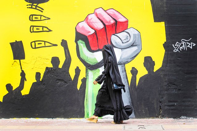 A woman walks past graffiti in Dhaka, Bangladesh, Friday, August 9, 2024. (Photo by Rajib Dhar/AP Photo)